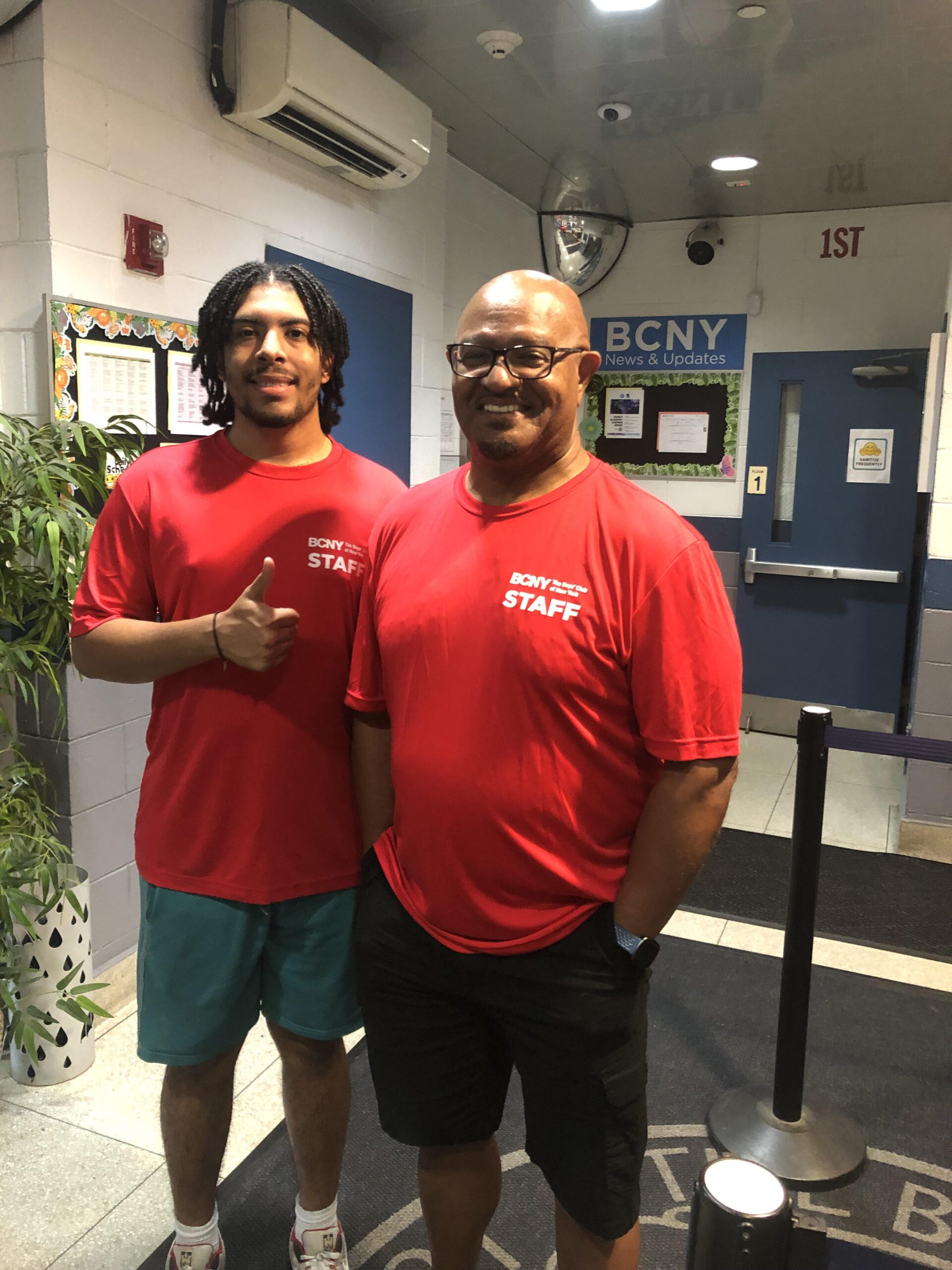 Carlos Vicente Sanchez and Ron Britt stand smiling in BCNY red staff shirts