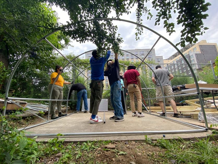 A group of students build a metal frame shaped like an arch for a greenhouse structure