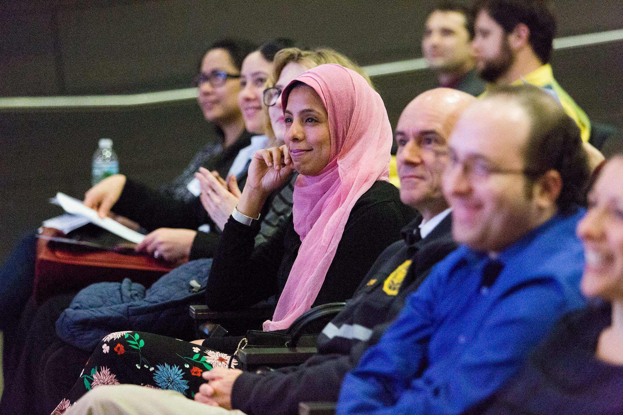 Women in pink scarf sitting smiling in lecture hall