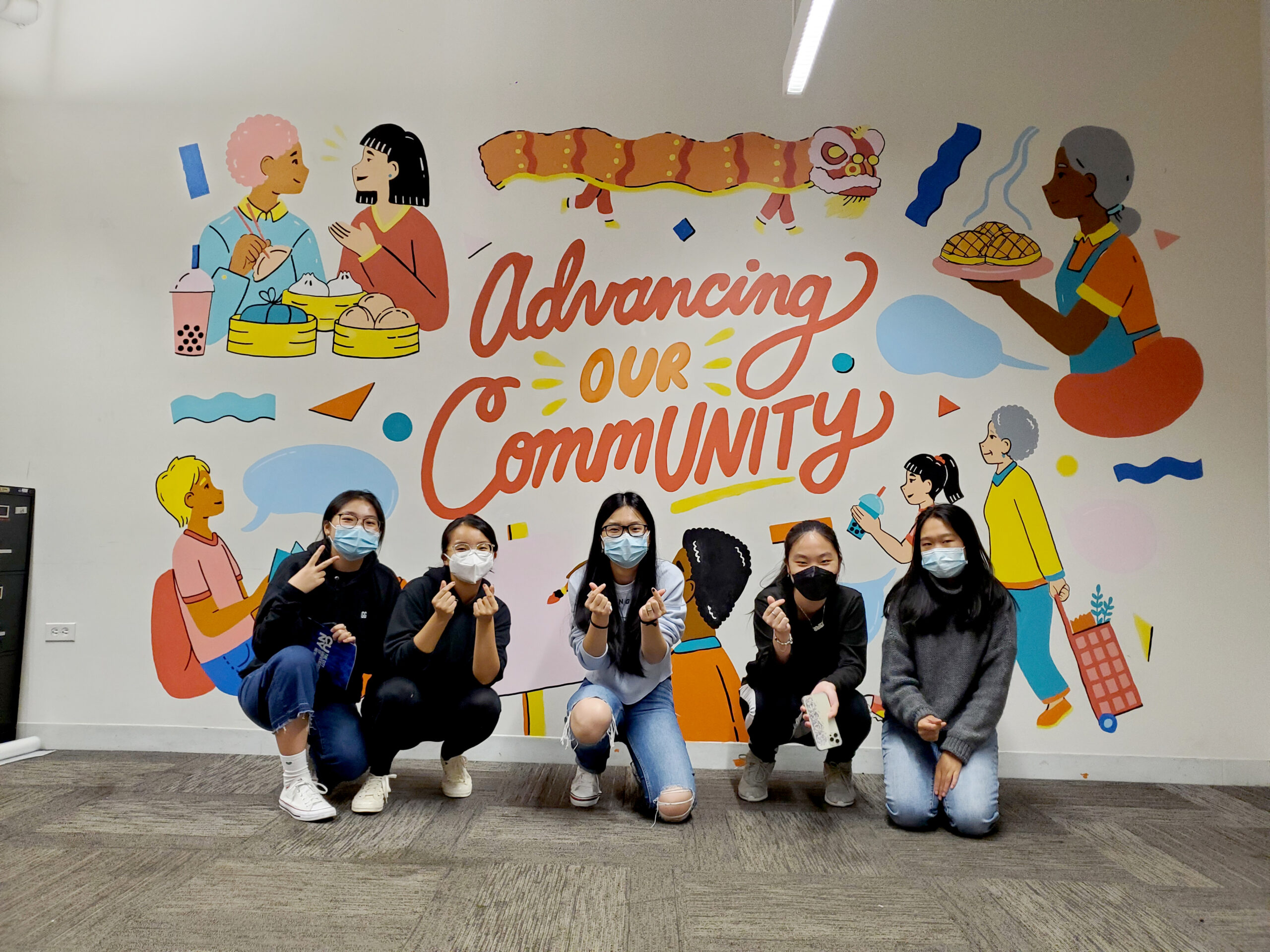 Students kneel in front of colorful mural that says Advancing our Community