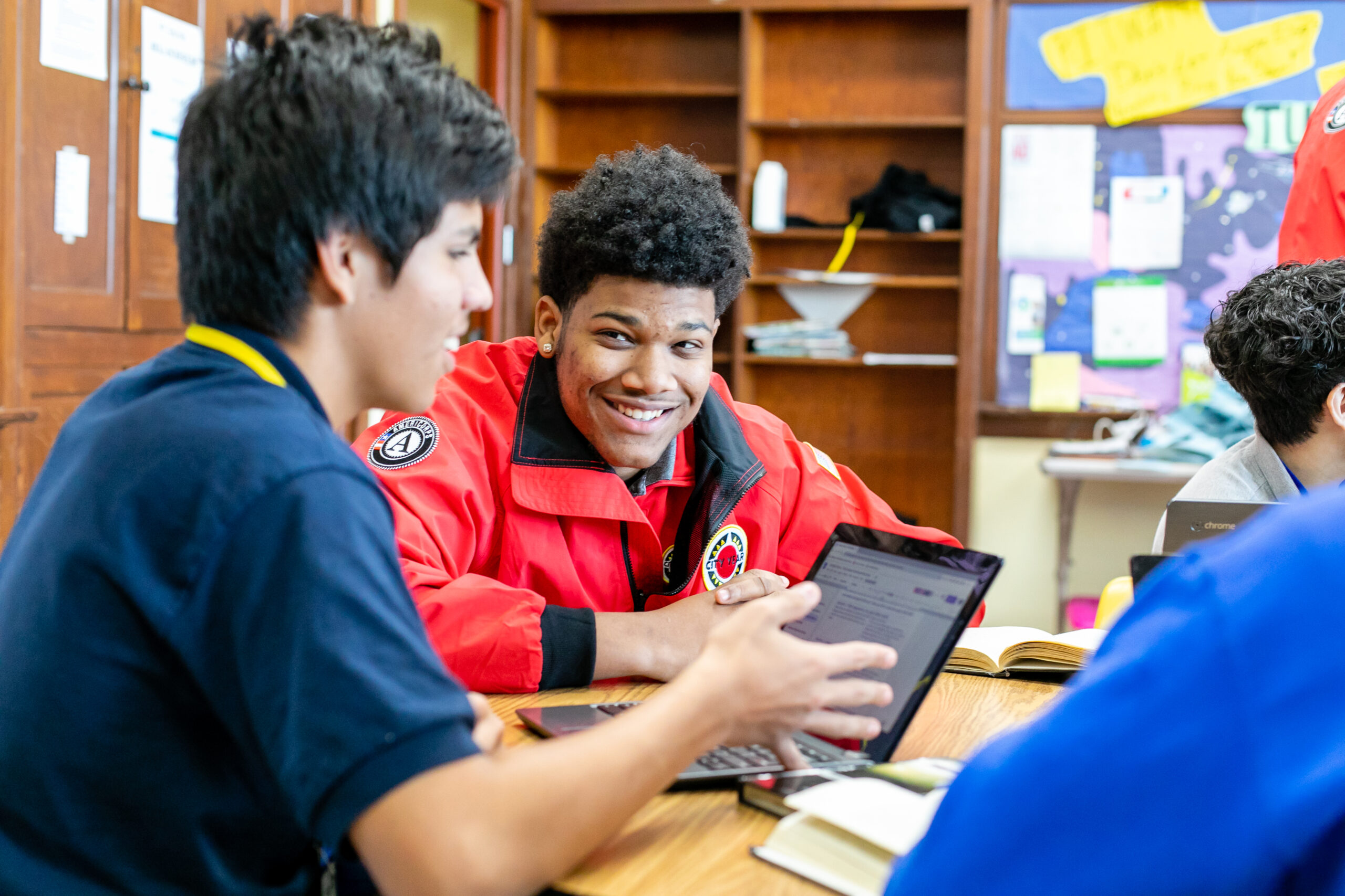 CYNY AmeriCorps Member smiles and sits with a student in front of a laptop doing schoolwork