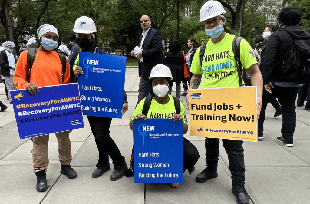 Folks in hardhats and neon shirts hold signs that say Fund Jobs and Training Now
