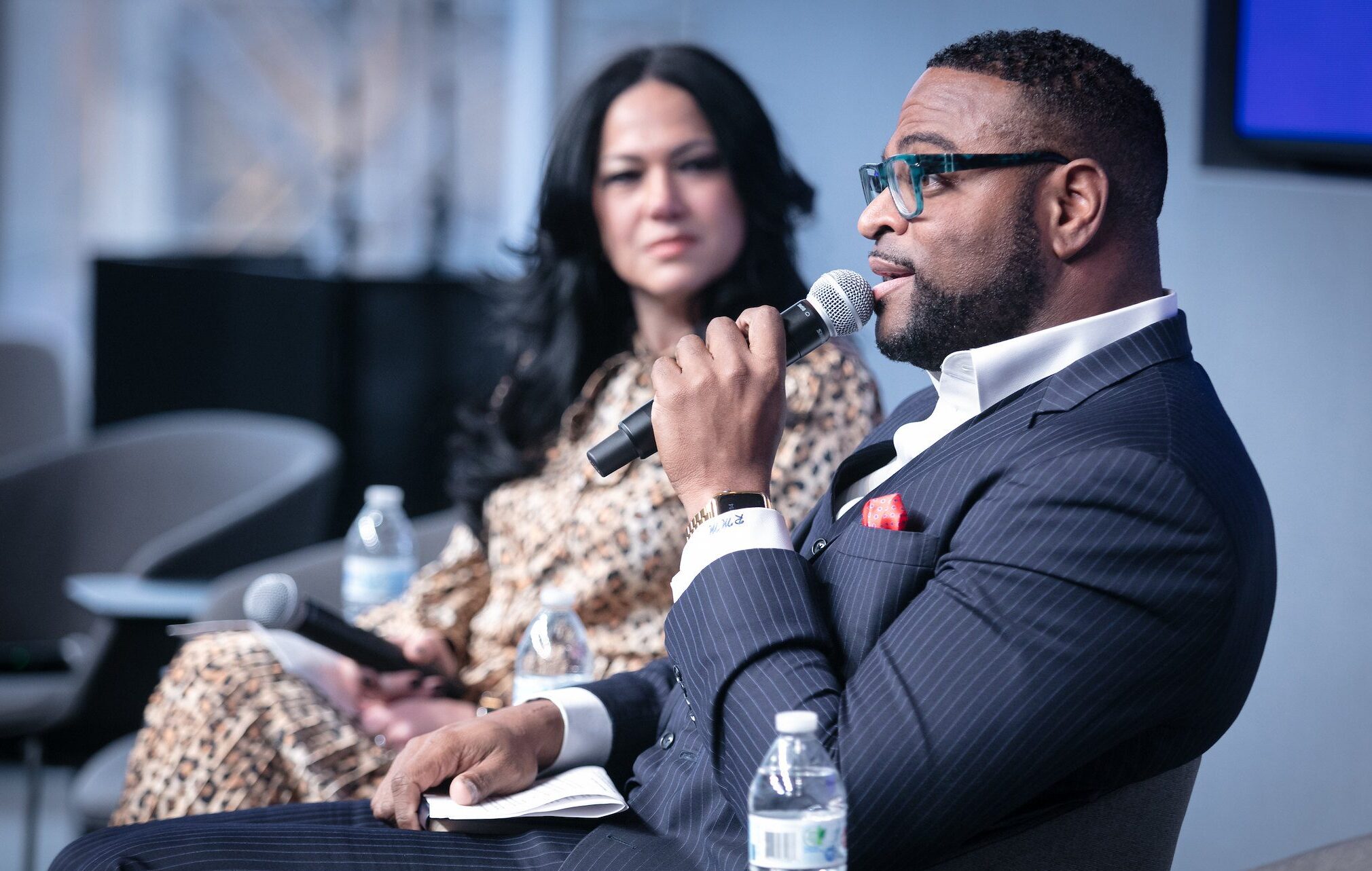 Two panelists on stage with one speaking into the microphone.