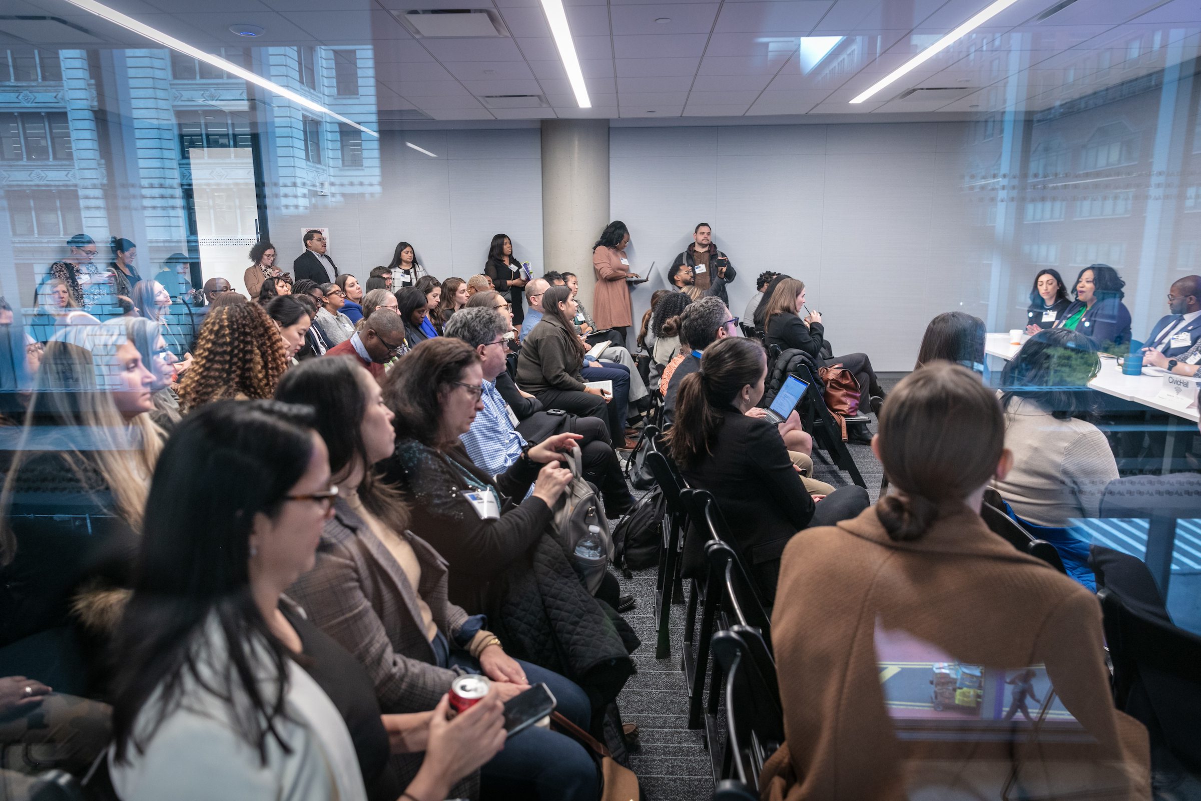 Professionals sit in a classroom listening to a panel discussion with a glass wall at Civic Hall.