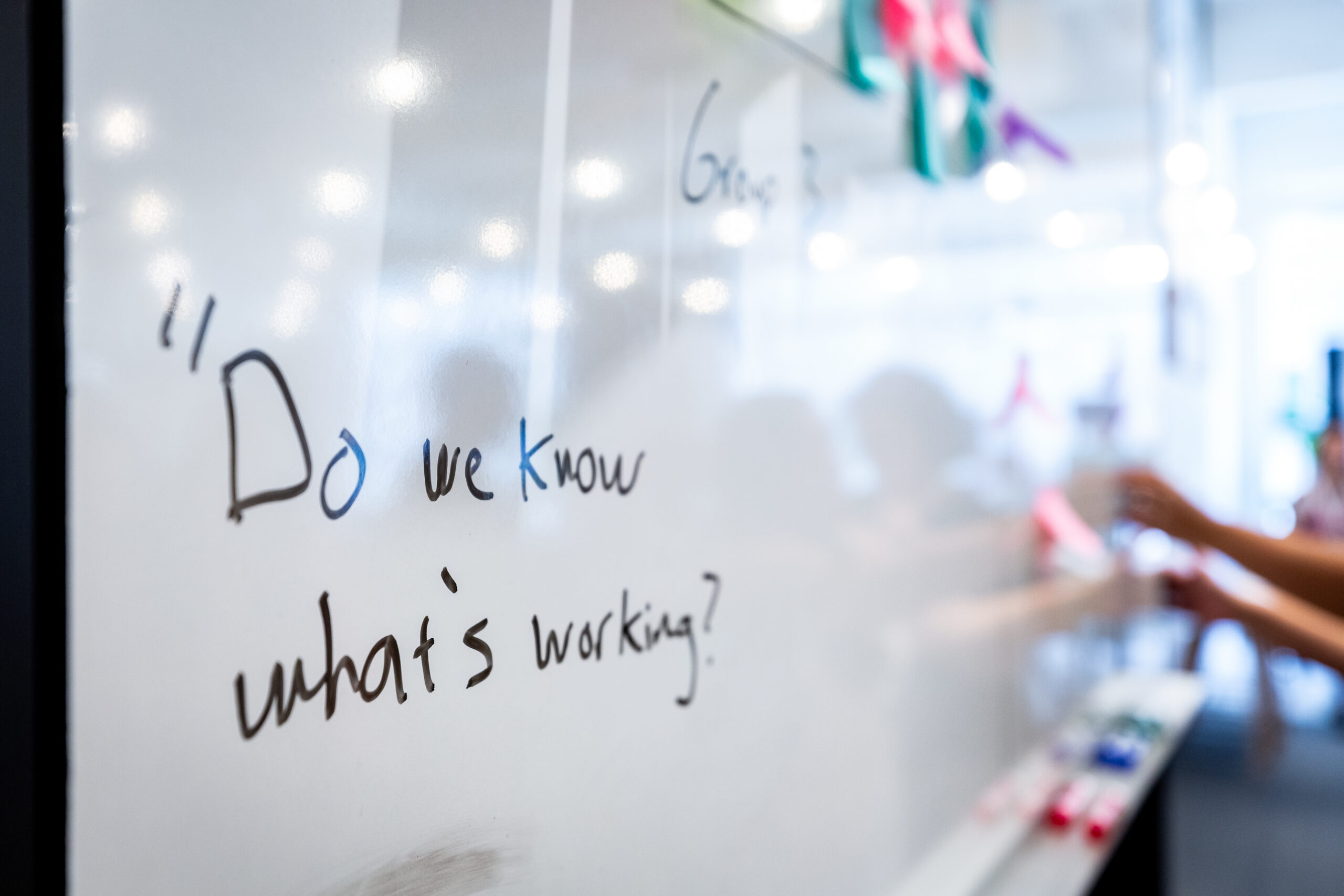 A whiteboard with cursive words written in black dry erase "Do we know what's working"