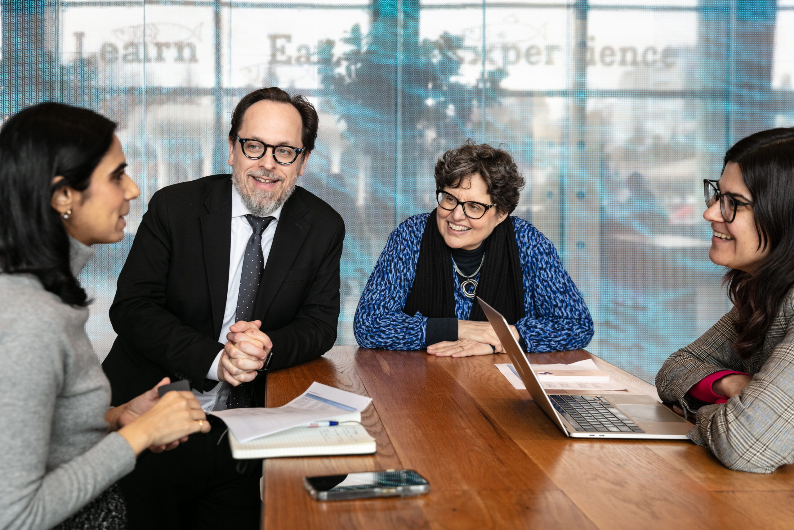 A group of four professionals smiling in front of computers and papers on a wooden table
