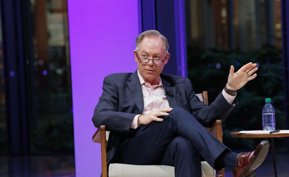 Randy Peers in a light shirt and blue suit seated on stage at The Times Center.