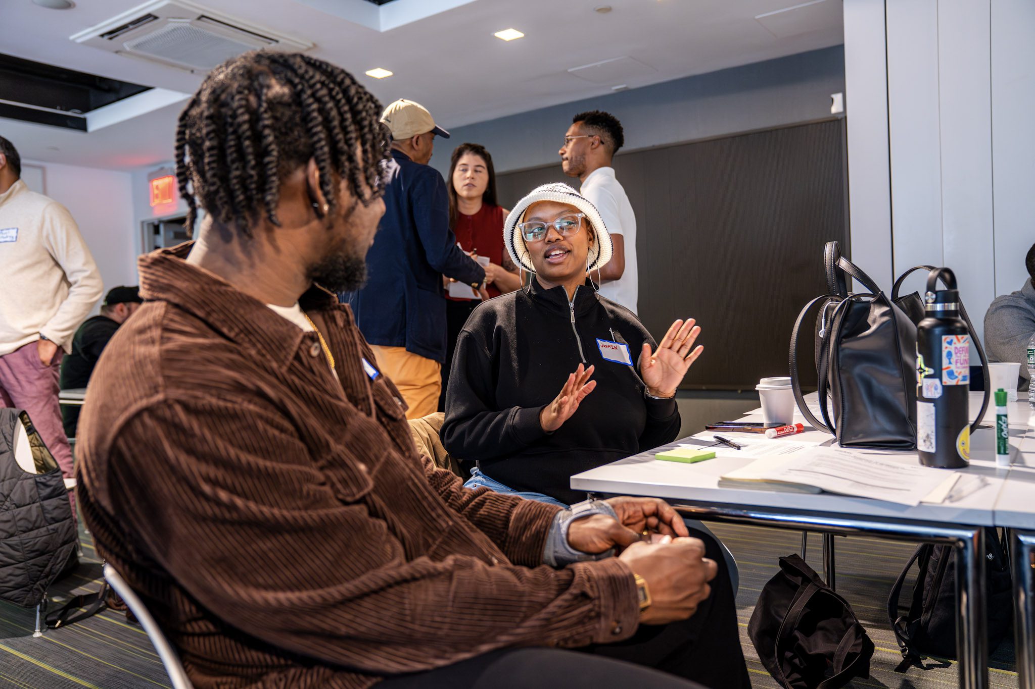 A Black woman in a black shirt and white knit bucket hat at the Workforce Benchmarking Meeting.