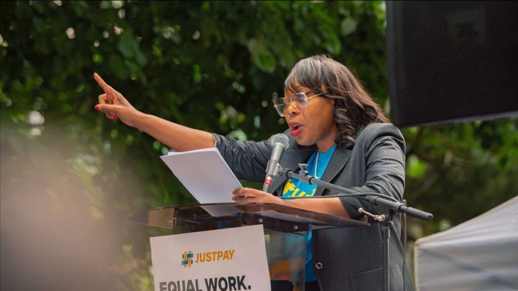 Sharon Sewell-Fairman speaks at the podium with arm raised up at the Just Pay rally.