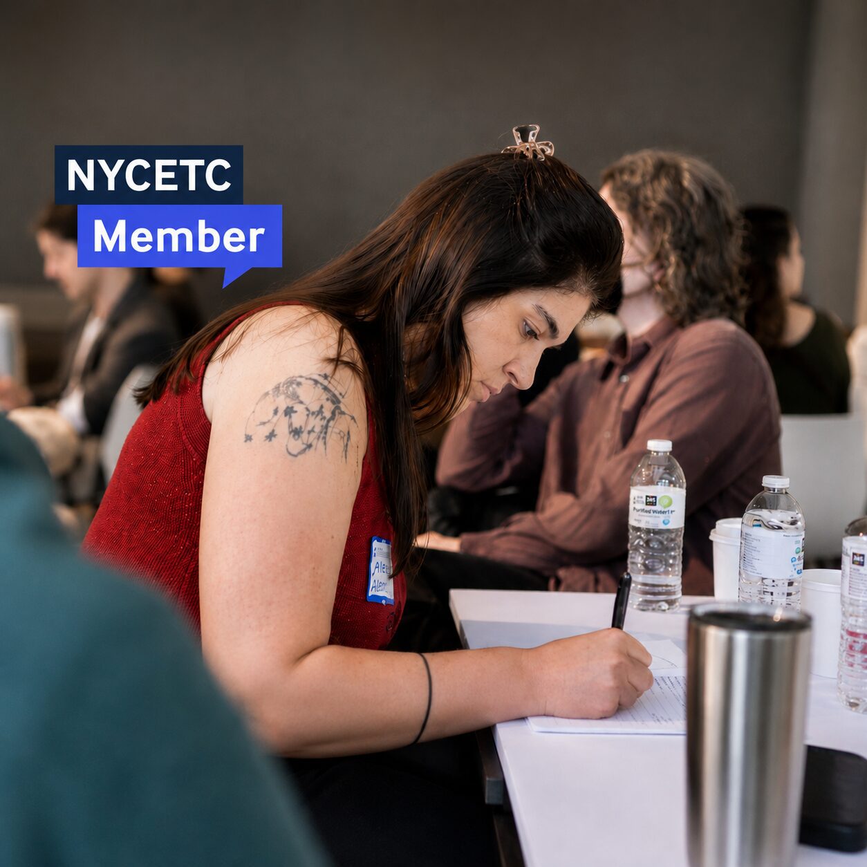 A photo of a seated woman in a red tank top writing on a piece of paper at a peer forum on workforce benchmarking.