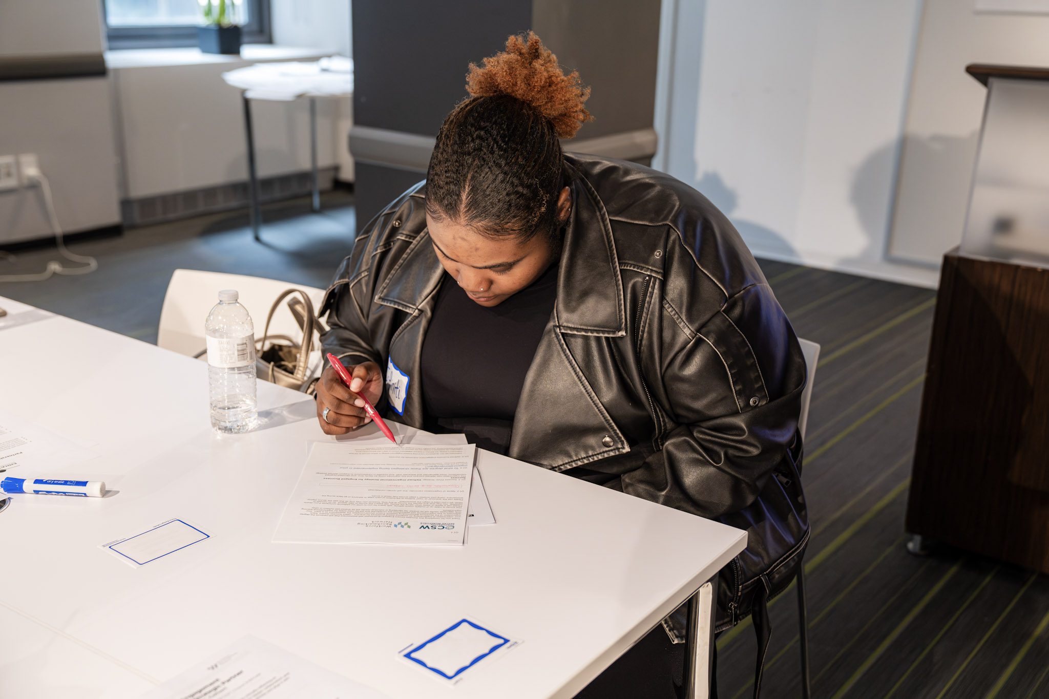 A woman with dark hair pulled back wearing all black sits at a table completing an assignment.