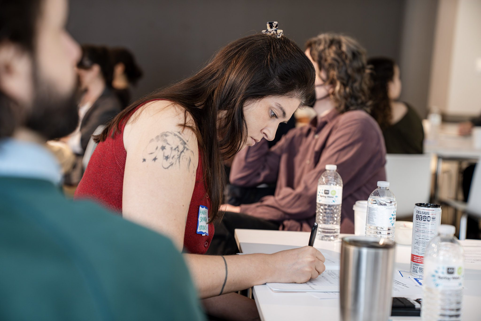 A photo of a seated woman in a red tank top writing on a piece of paper at a peer forum on workforce benchmarking.
